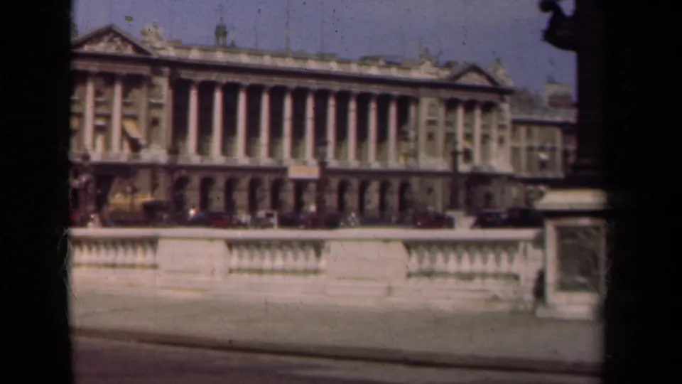 1939 Paris home-movie frame showing the building from a slightly shifted angle, with columns, balustrade, roadway, and period cars.