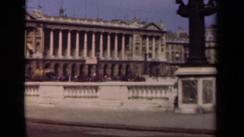 1939 Paris frame with the classical building, foreground stonework, parked cars, and a dark street lamp at the right edge.