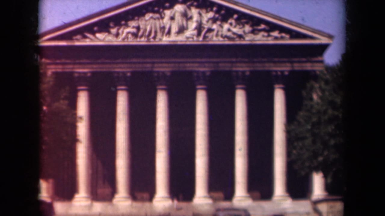 Paris landmark facade, likely La Madeleine, seen in soft 8mm color with tall columns, pediment sculpture, and trees at the edge.