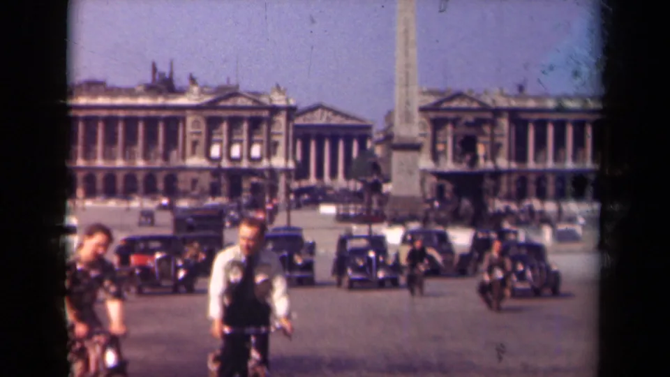 1939 Paris street scene with two cyclists near the foreground, period cars behind them, and the obelisk rising in Place de la Concorde.