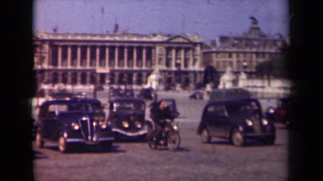 1939 Paris home-movie frame showing vintage automobiles, a rider, pedestrians, and grand architecture across a public square.