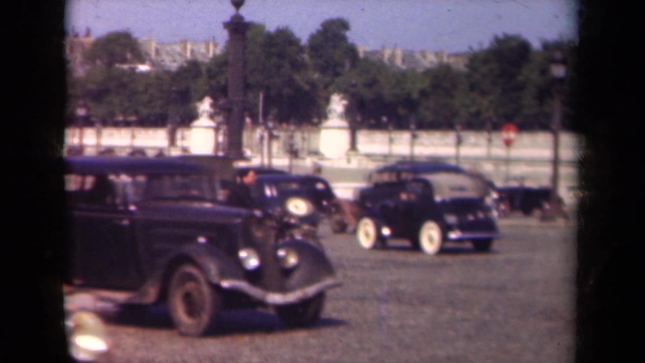 1939 Paris street scene with old automobiles, a cyclist, pedestrians, trees, and distant architecture near Place de la Concorde.