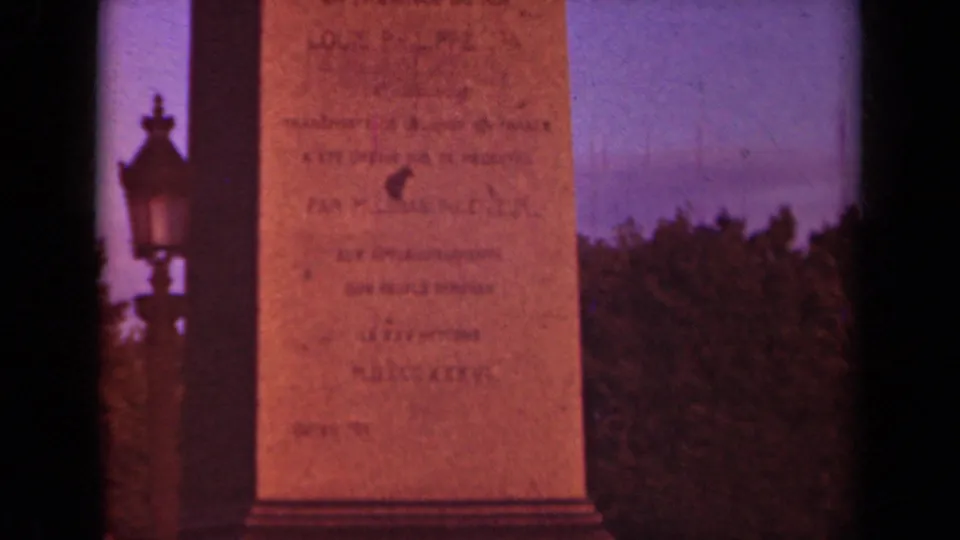 Close 1939 Paris home-movie view of an inscribed monument face with an ornate lamp, trees, and purple-blue sky.