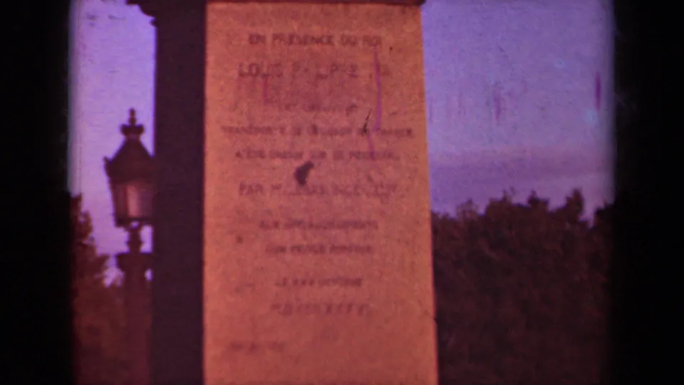 Paris monument detail from the 1939 8mm clip, showing inscription lines, a street lamp silhouette, trees, and warm faded color.