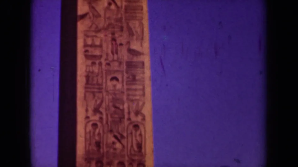 Paris travel footage frame showing the lower carved obelisk shaft, bordered by a dark lamppost and 8mm frame edges.