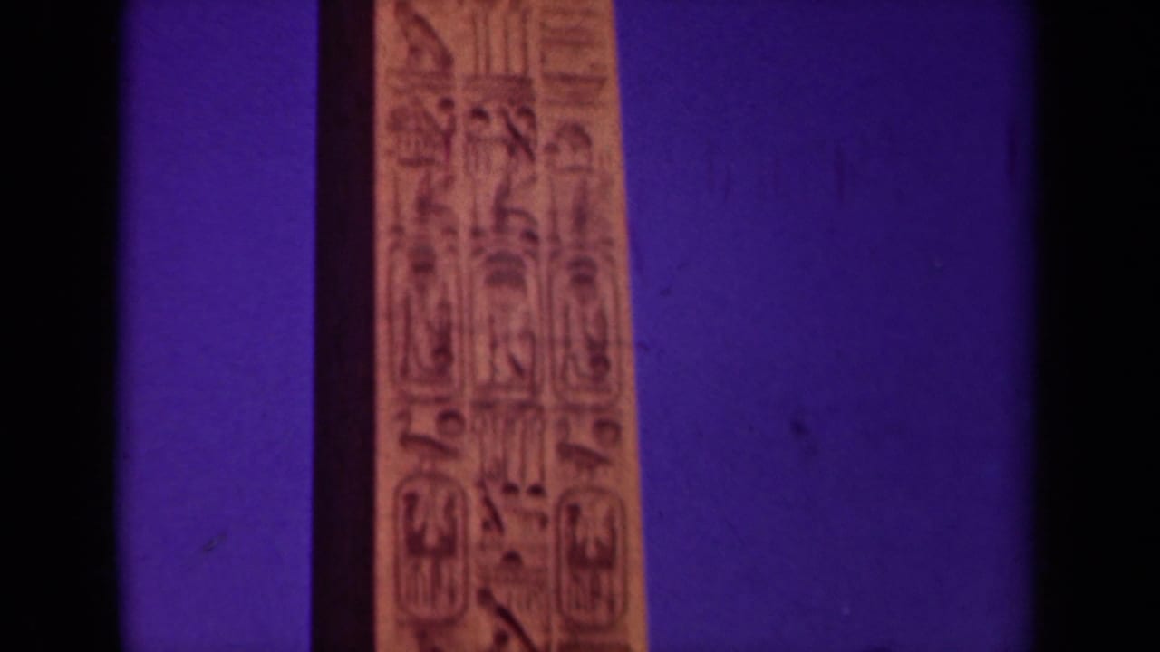 1939 Paris travel footage frame showing the upper section of a tan obelisk with carved hieroglyph-like markings against saturated purple.