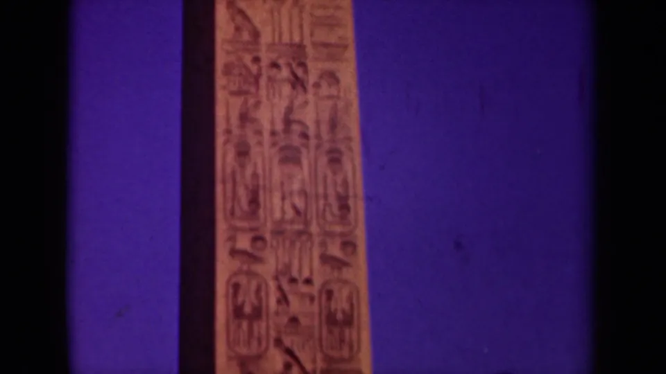 1939 Paris travel footage frame showing the upper section of a tan obelisk with carved hieroglyph-like markings against saturated purple.