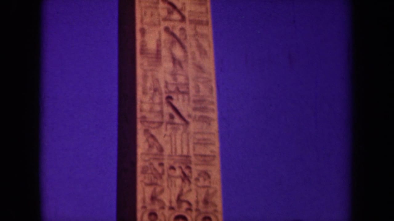 Narrow obelisk face with carved symbols centered beside dark film borders.
