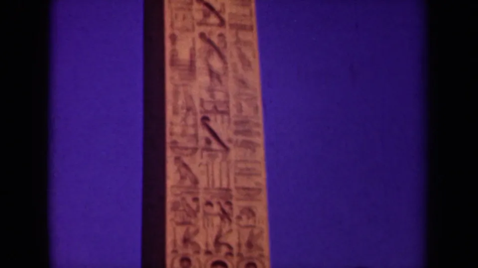 1939 Paris frame with a narrow obelisk face carrying carved Egyptian-style symbols, bordered by dark scan edges and purple color cast.