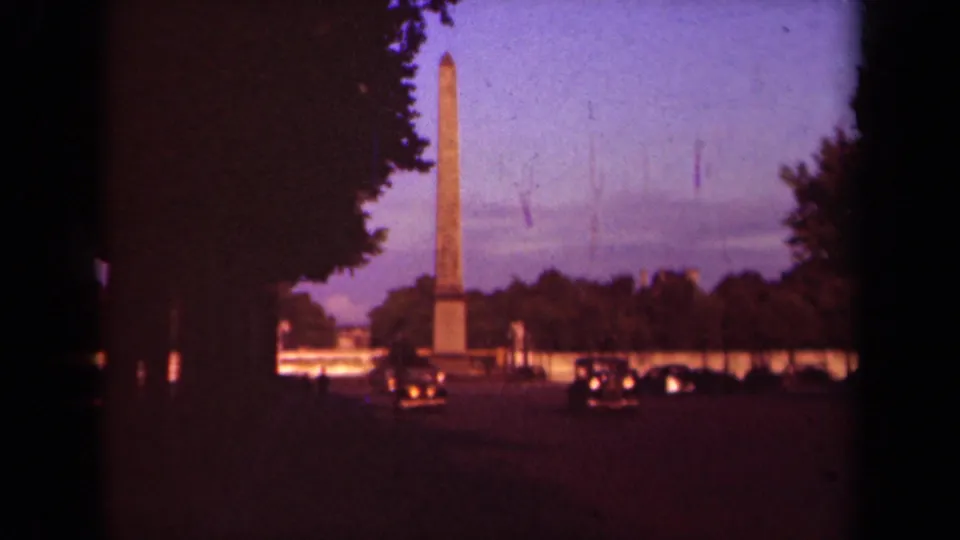 Wide 1939 Paris street view showing an obelisk beyond dark trees, low buildings, and classic cars with headlights.