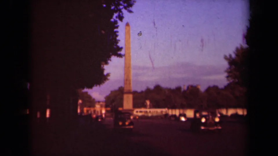 Late-1930s Paris view of an obelisk at twilight, with classic automobiles and dark tree silhouettes in the foreground.