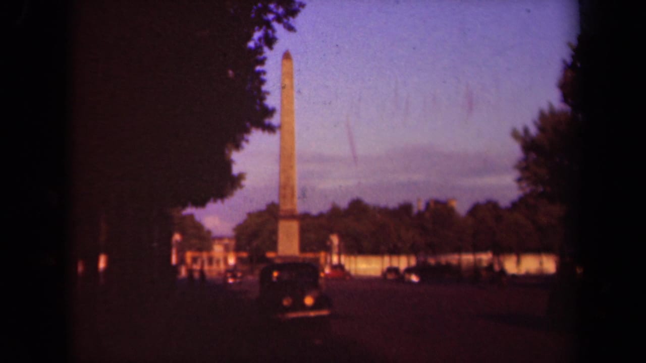 Obelisk and surrounding traffic seen through a dark tree-framed street view.