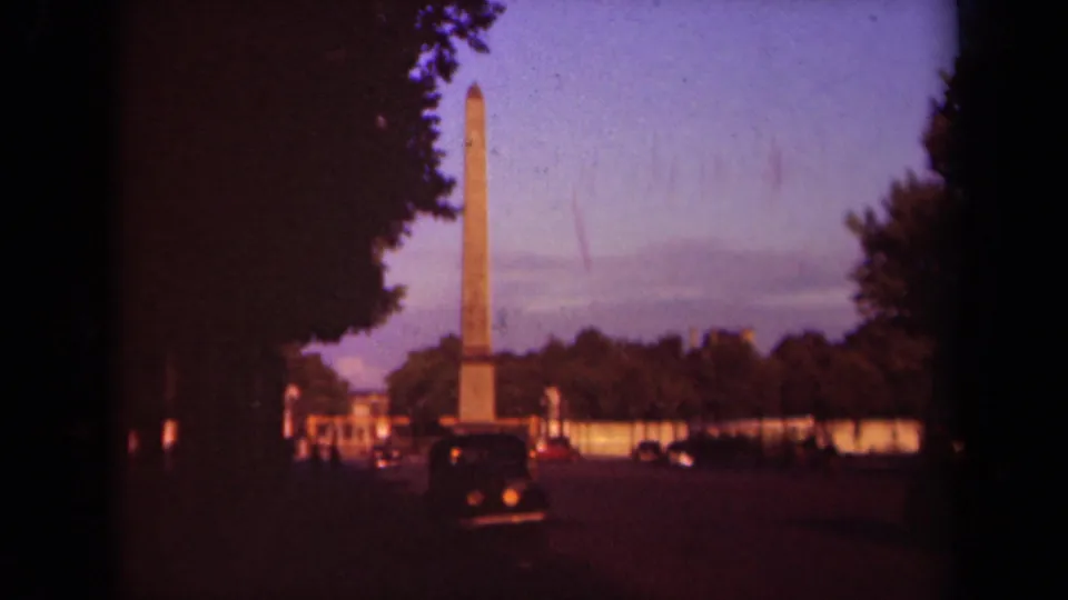 Paris landmark view from 1939 footage, with the obelisk centered beyond cars, trees, and a purple dusk sky.