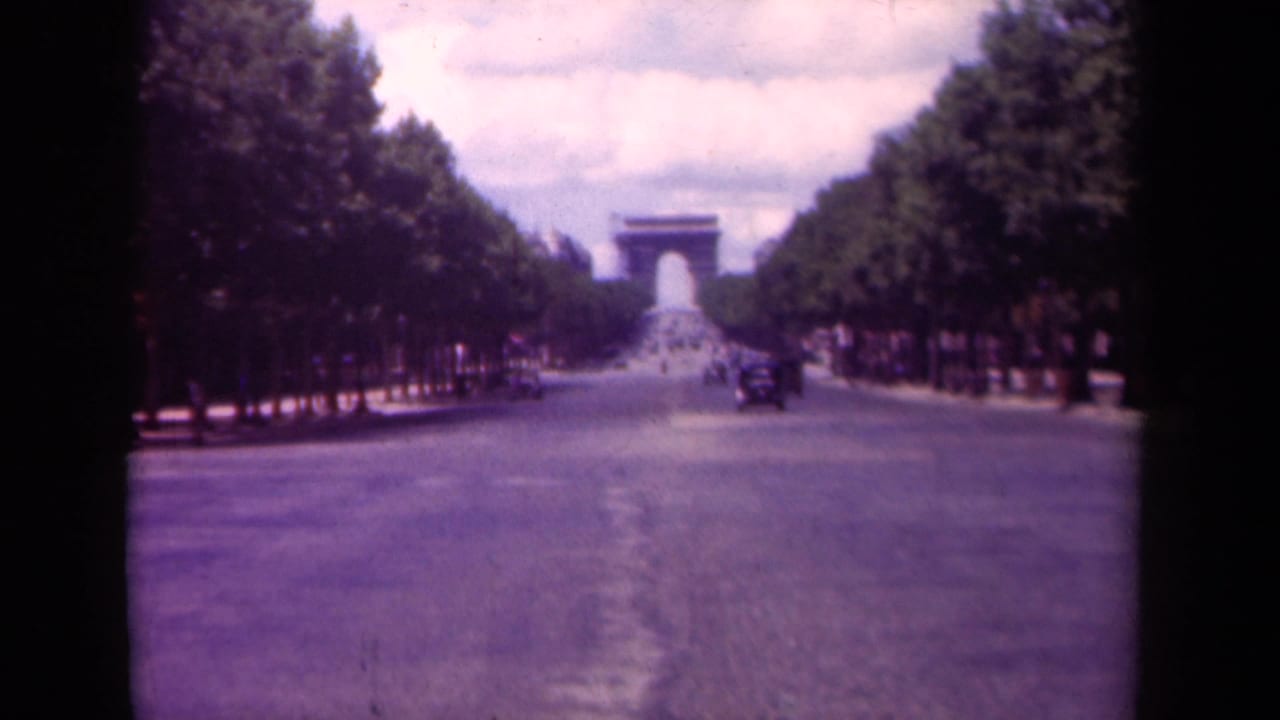 Tree-lined Paris avenue with the Arc de Triomphe in the distance and a car on the roadway.