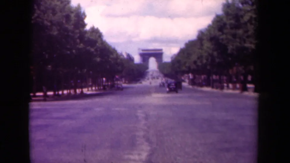 1939 8mm view down the Champs-Elysees toward the Arc de Triomphe, with trees flanking the broad road and sparse traffic.
