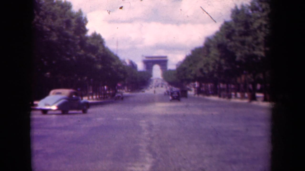 Antique car crosses the foreground on a broad avenue leading toward the Arc de Triomphe.