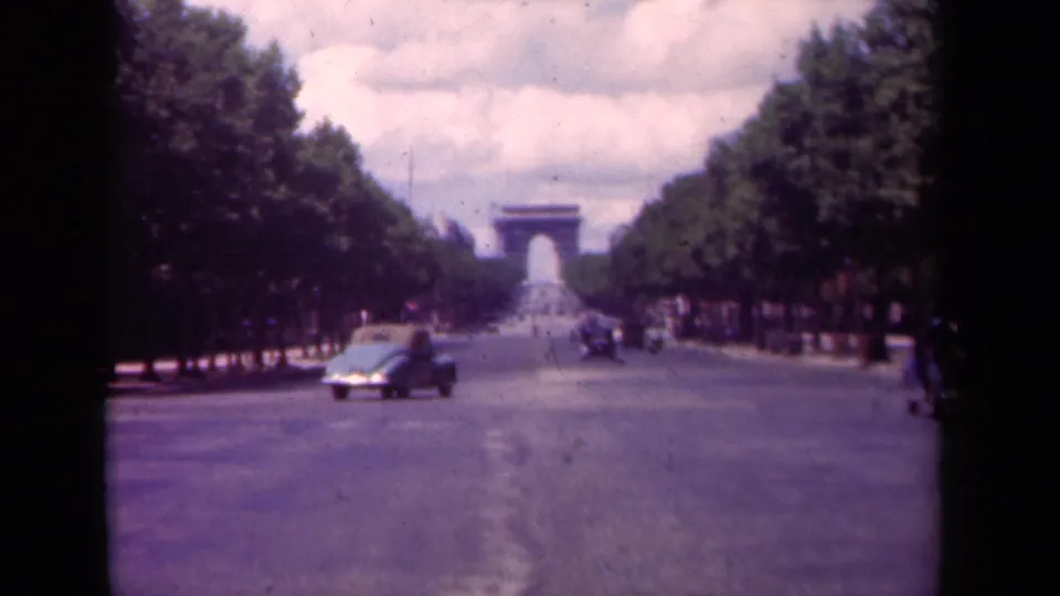 The Champs-Elysees appears from a low visitor viewpoint, with an antique car crossing the near lane and the Arc de Triomphe in soft focus.