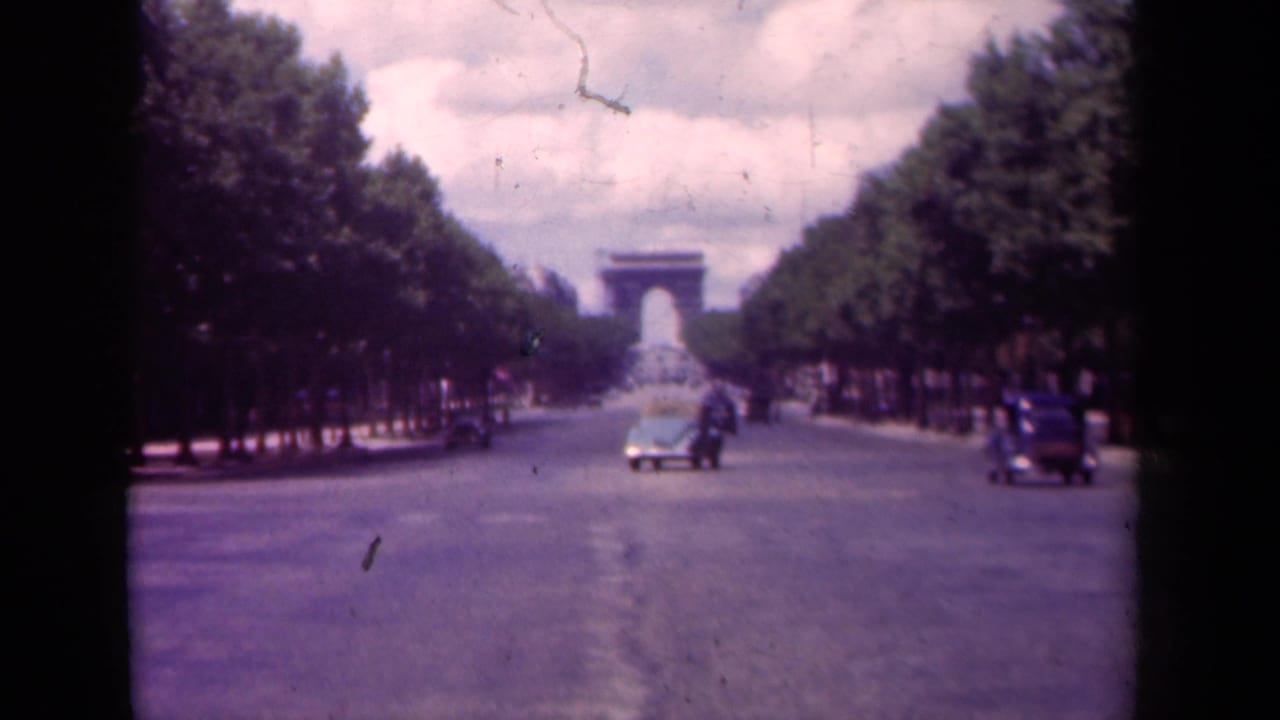 1939 Paris home-movie frame showing the Arc de Triomphe beyond the Champs-Elysees, with classic cars and pedestrians on the avenue.