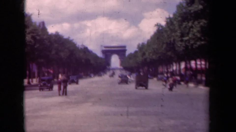 1939 Paris frame looking down the Champs-Elysees toward the Arc de Triomphe, with pedestrians in the roadway and cars along both sides.
