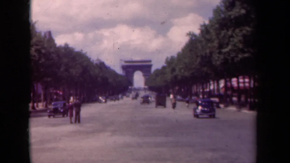 Soft 8mm frame of the Champs-Elysees facing the Arc de Triomphe, showing light traffic and pedestrians in a travel-film view.
