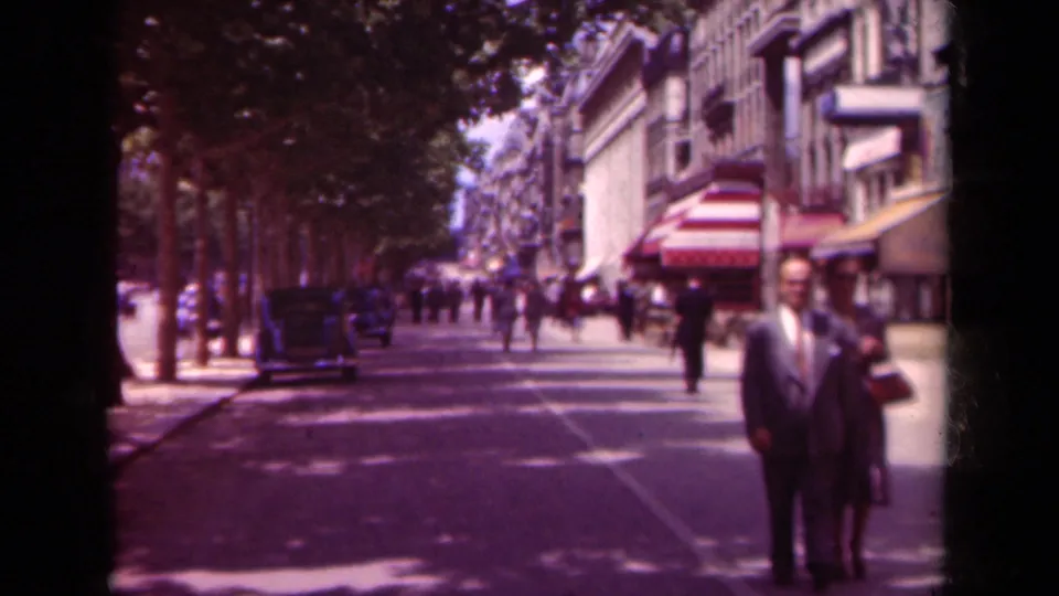 In the stated 1939 Paris scene, the couple is near the foreground on a broad tree-lined street with awnings, storefronts, and distant foot traffic.