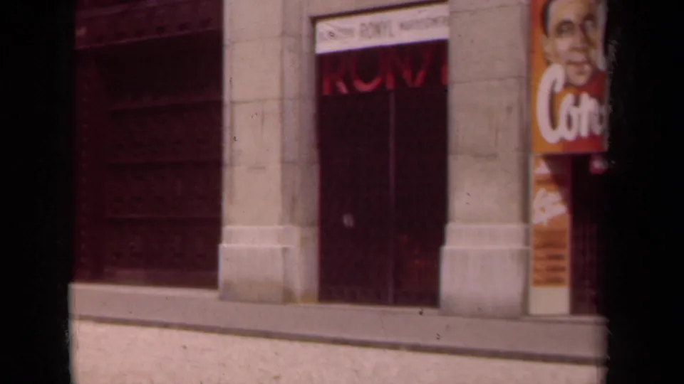 1939 Paris frame with the camera passing the cinema frontage, leaving the poster partly cropped beside a red door and stone wall.
