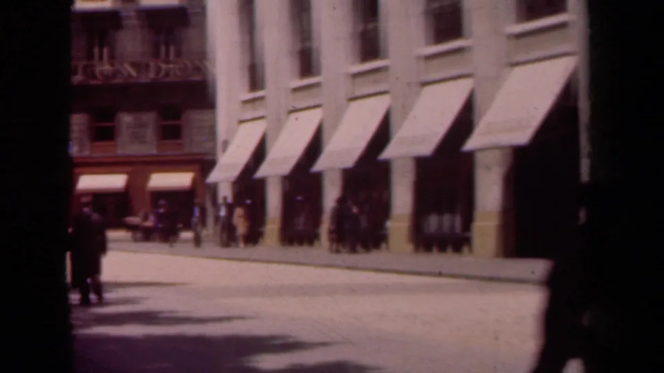 1939 Paris shopfront row with awnings, pedestrians, and visible 8mm gate edge during a street pan.