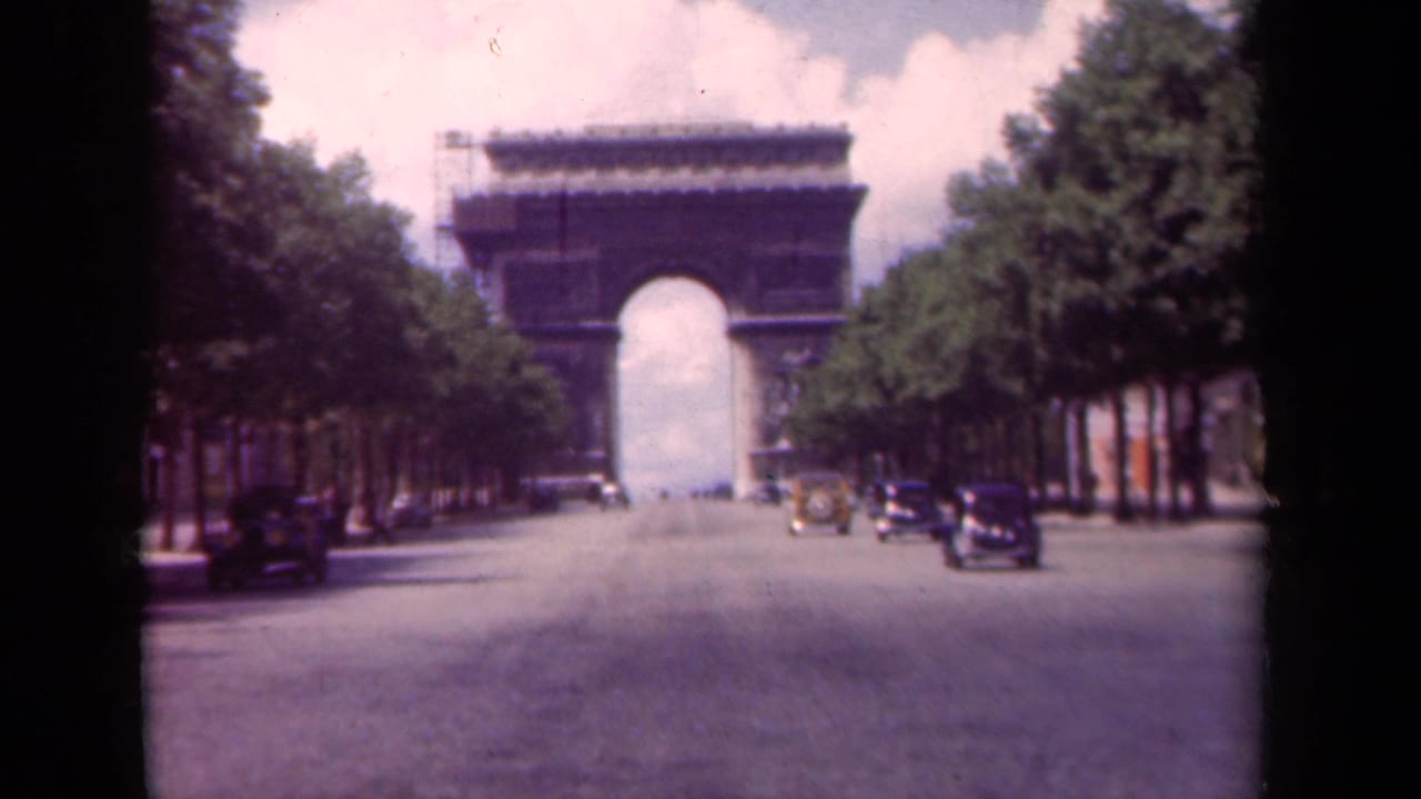 1939 Paris home-movie frame showing the Arc de Triomphe beyond the Champs-Elysees, with vintage cars and trees lining the road.