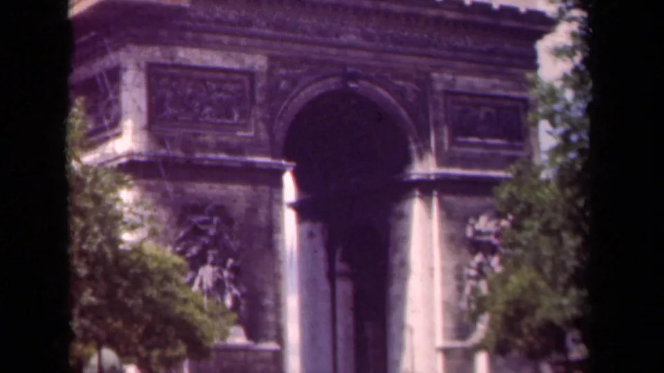 1939 Paris home-movie frame showing the Arc de Triomphe central arch, sculptural reliefs, and trees along the edge.