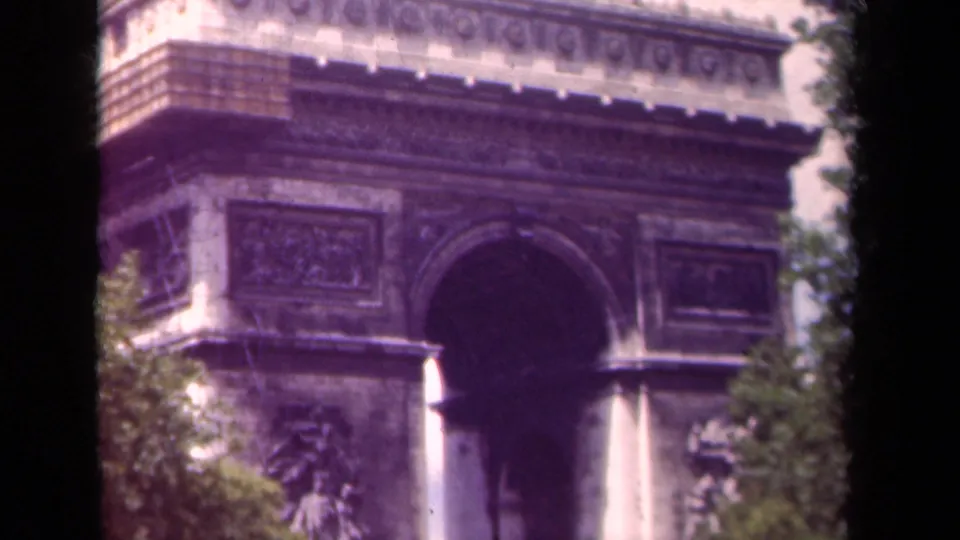 1939 8mm frame of the Arc de Triomphe facade in Paris, with relief sculpture, trees, and soft magenta film color.