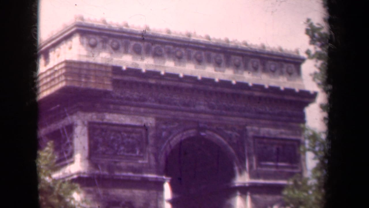 The Arc de Triomphe in Paris appears in soft color 8mm footage with trees and dark film edges visible.