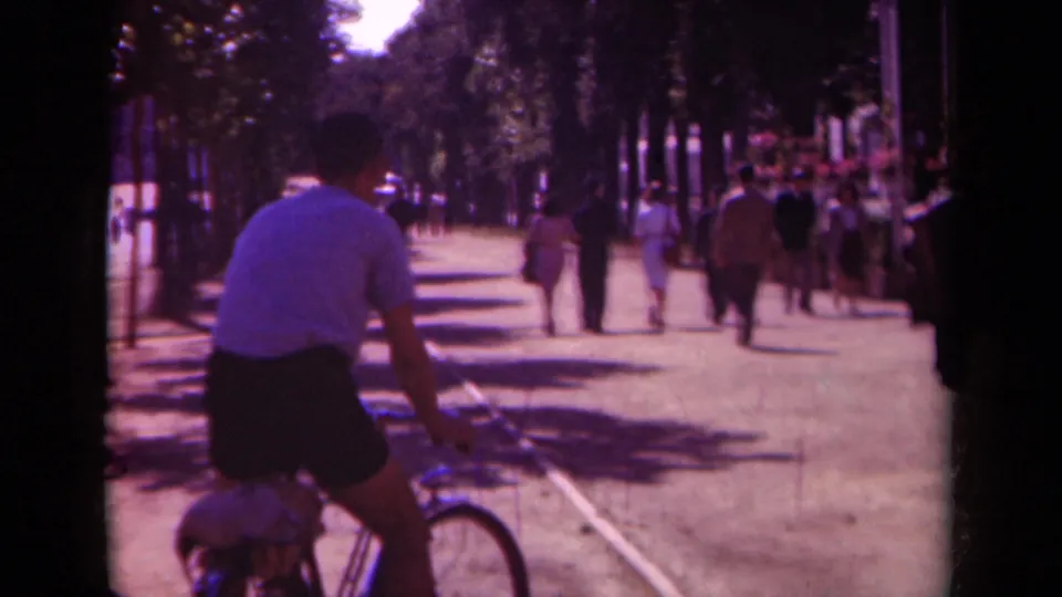 1939 Paris street scene with a bicyclist close to the camera and pedestrians moving along a shaded avenue.
