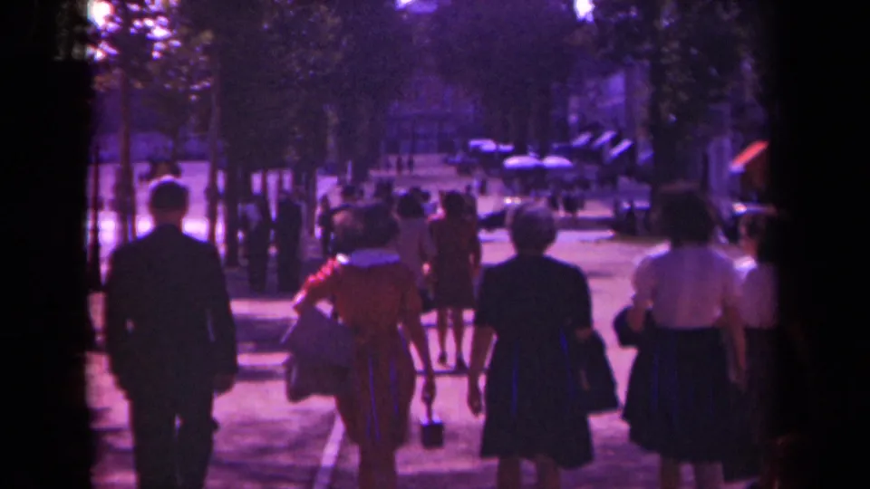 Adults in period clothing walk away along a Paris boulevard in a 1939 home-movie frame with strong color fading and grain.