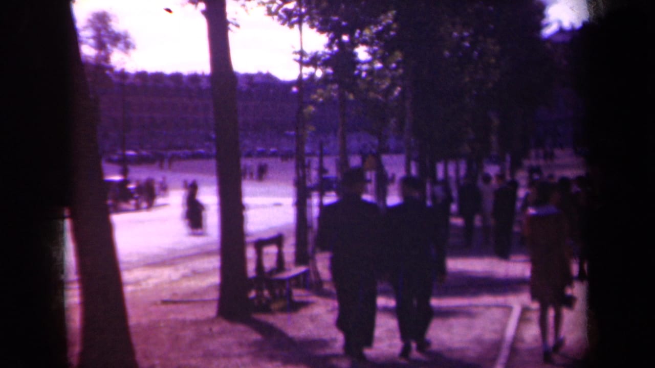 1939 Paris street scene with pedestrians walking away from the camera under trees near benches and a broad roadway.