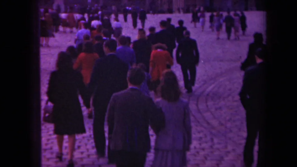 1939 Paris home-movie view of a dense pedestrian crowd walking away across cobblestones, with suits and dresses visible.
