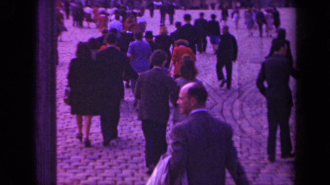 Paris 1939 home-movie frame showing people in suits and dresses walking across a cobblestone public square.