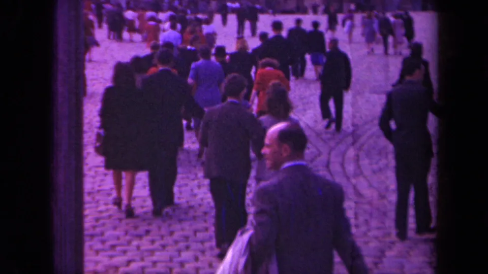 Paris 1939 home-movie frame showing people in suits and dresses walking across a cobblestone public square.
