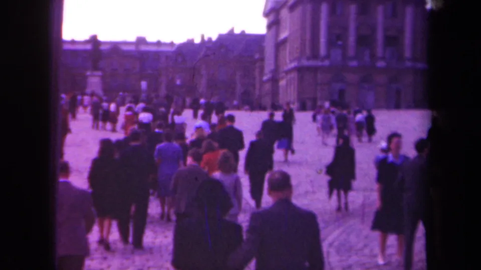 Paris 1939 home-movie frame of people walking across a cobblestone square beside large stone buildings.
