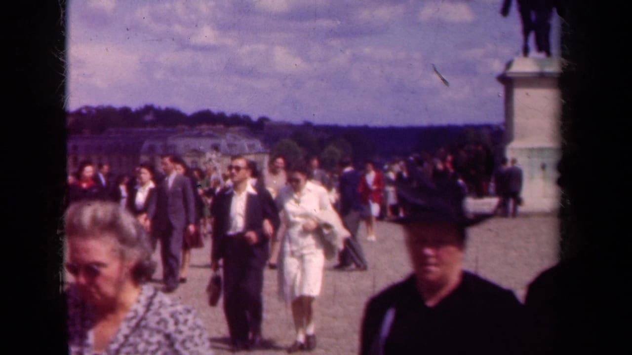 Pedestrians in formal clothing walk across a broad courtyard near a statue pedestal.