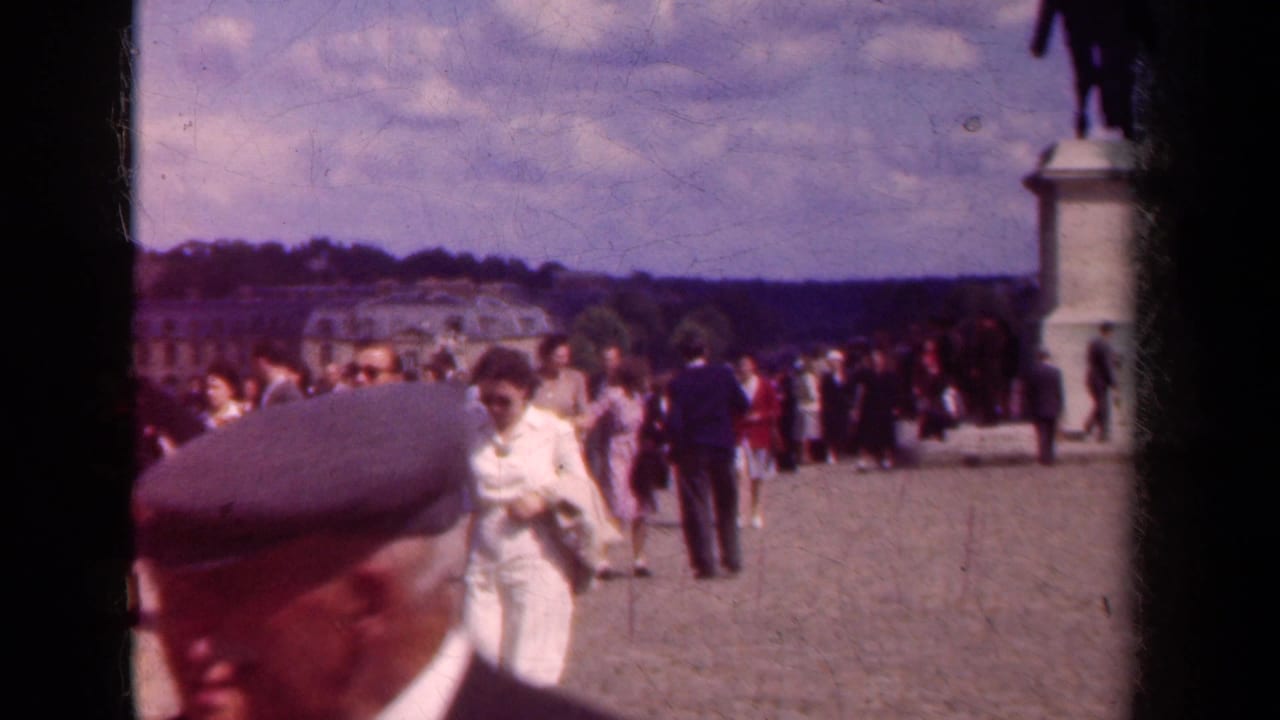 1939 France frame with a close passerby in a cap and many pedestrians moving through a public courtyard.