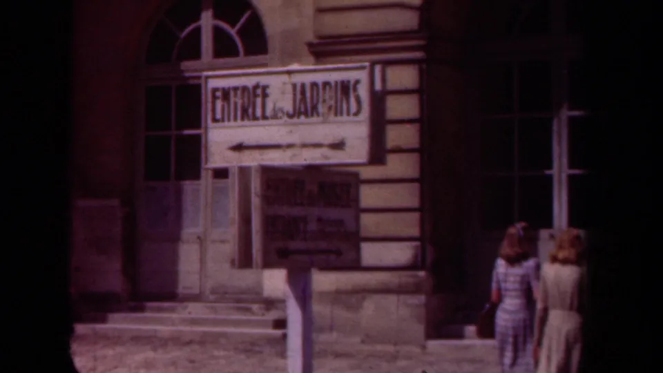 1939 France home-movie frame showing an “Entrée des Jardins” sign before a formal building entrance.