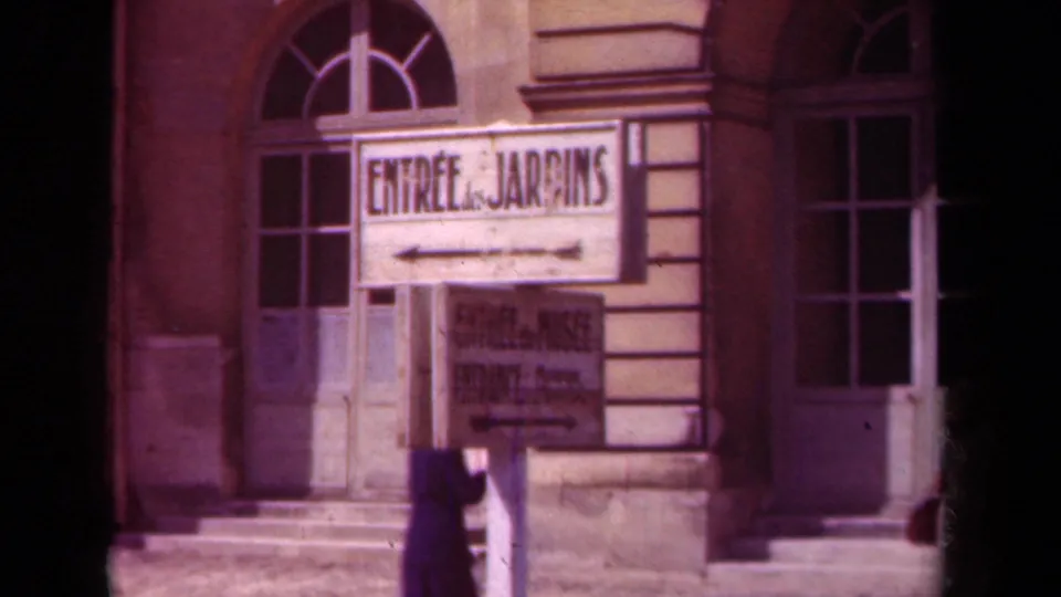 1939 France frame centered on the “Entrée des Jardins” sign outside a public garden or palace grounds entrance.