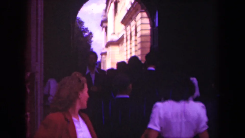 In 1939 Paris home-movie footage, tourists move through a shadowed arch toward sunlit buildings beyond.