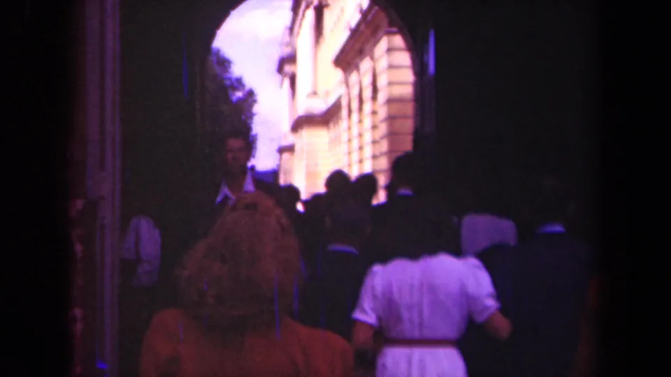 Visitors seen from behind enter a sunlit Paris courtyard through a dark arched gateway in 1939 8mm footage.