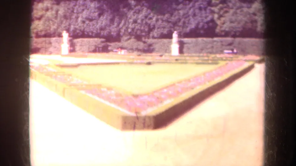 A formal Paris garden appears in soft 8mm color, with geometric flowerbeds, clipped borders, pale walkways, and white statues.