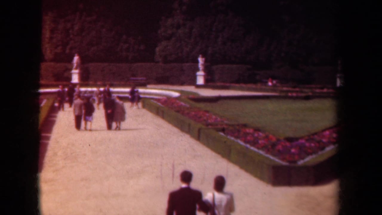 1939 Paris home-movie frame showing visitors strolling on a wide garden path with red flowerbeds, lawns, clipped hedges and white statues.