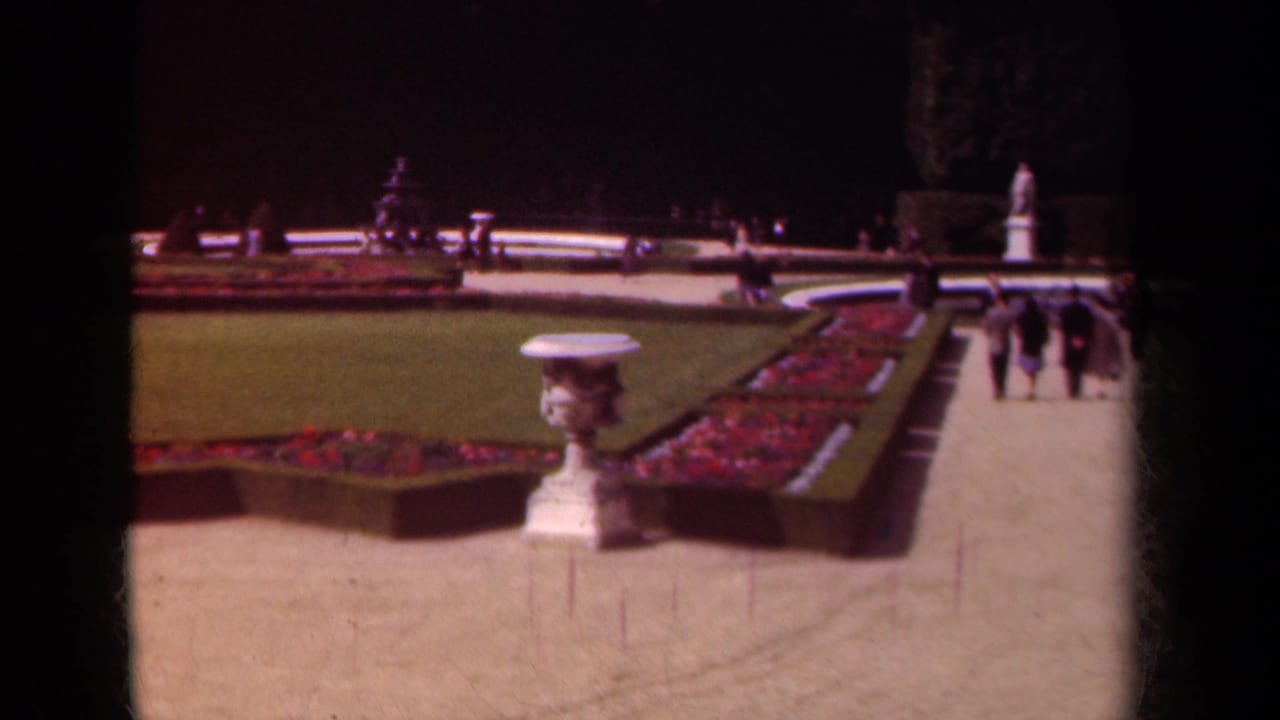 1939 Paris garden view with manicured beds, a pale urn, gravel walkways, distant visitors, and formal statuary beyond the lawn.