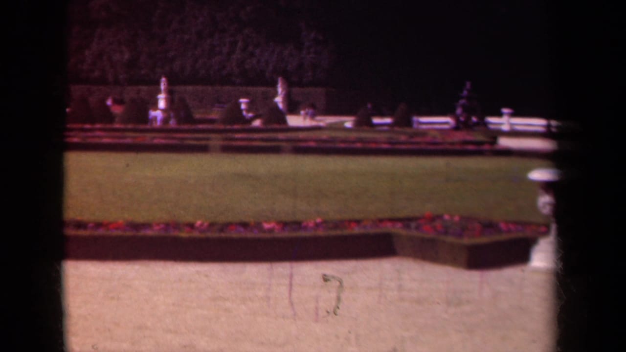 A 1939 Paris garden view shows a manicured lawn, long flower border, stone ornaments, and a dark vertical obstruction in the frame.