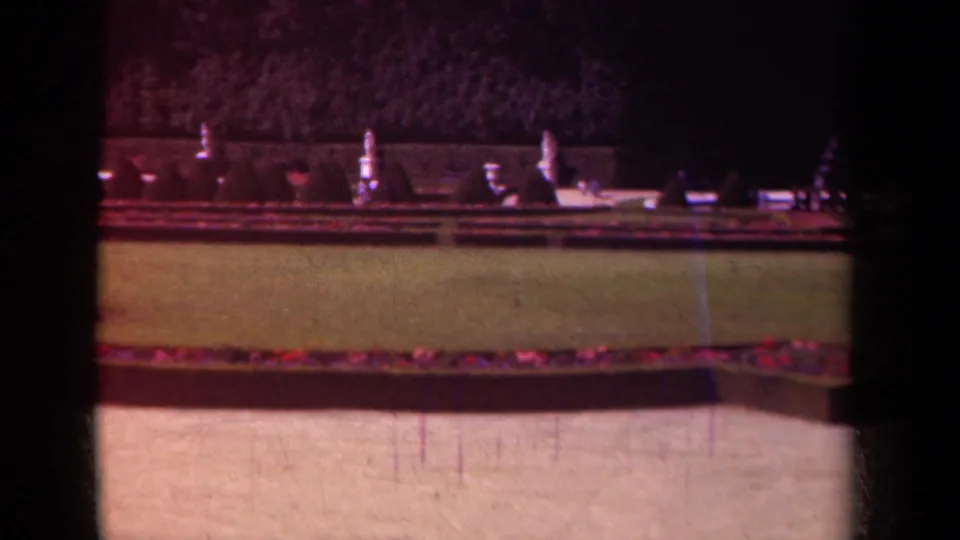 The 1939 Paris garden pan passes a low wall and clipped lawn, with red planting beds and pale stone ornaments in the background.