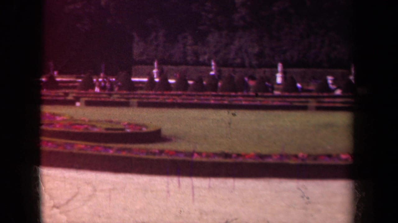 1939 Paris frame of manicured grounds with circular planting beds, lawn, low hedges, and dark trees in soft 8mm color.